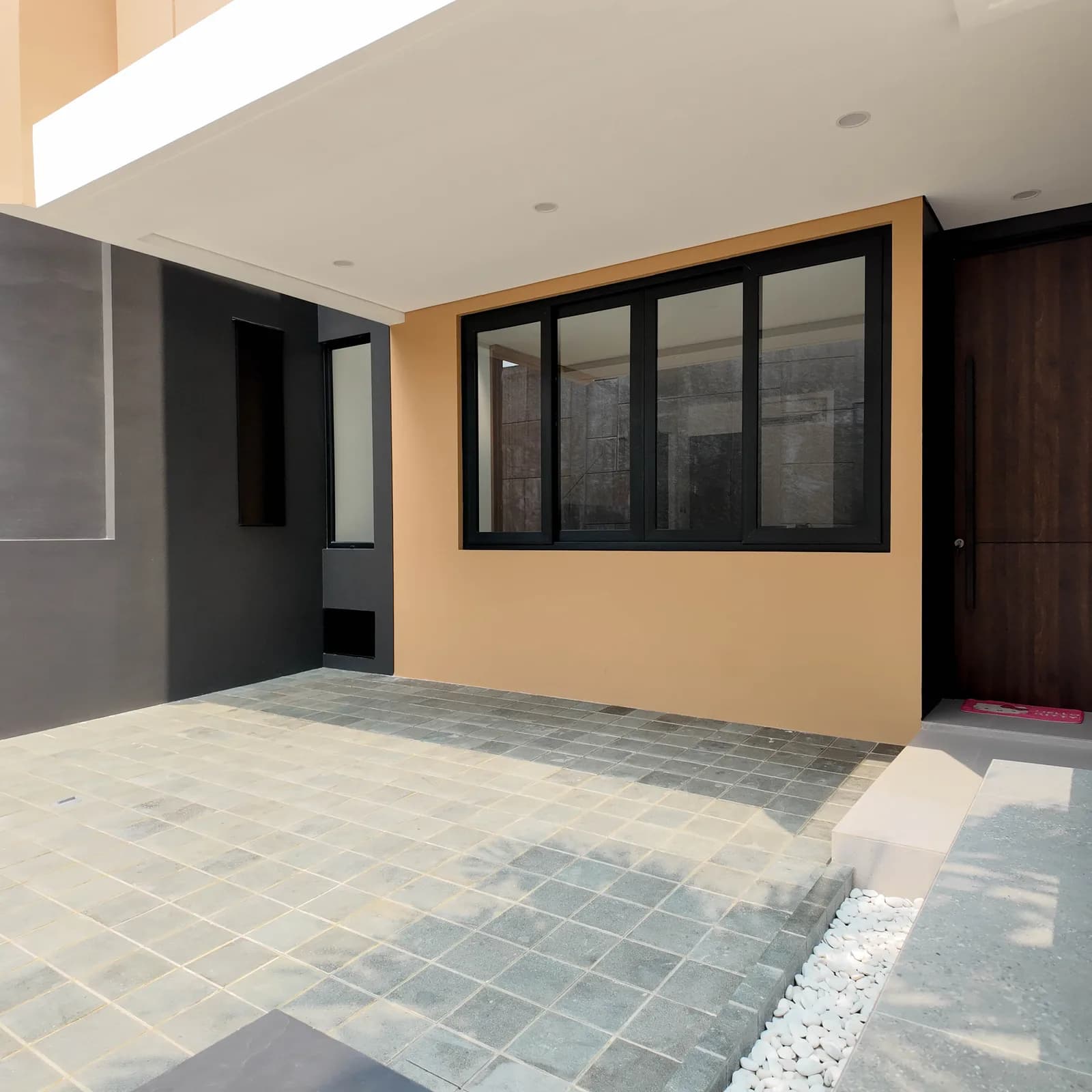 Photograph of a finished carport under its flat cantilevered canopy, beside the timber front door