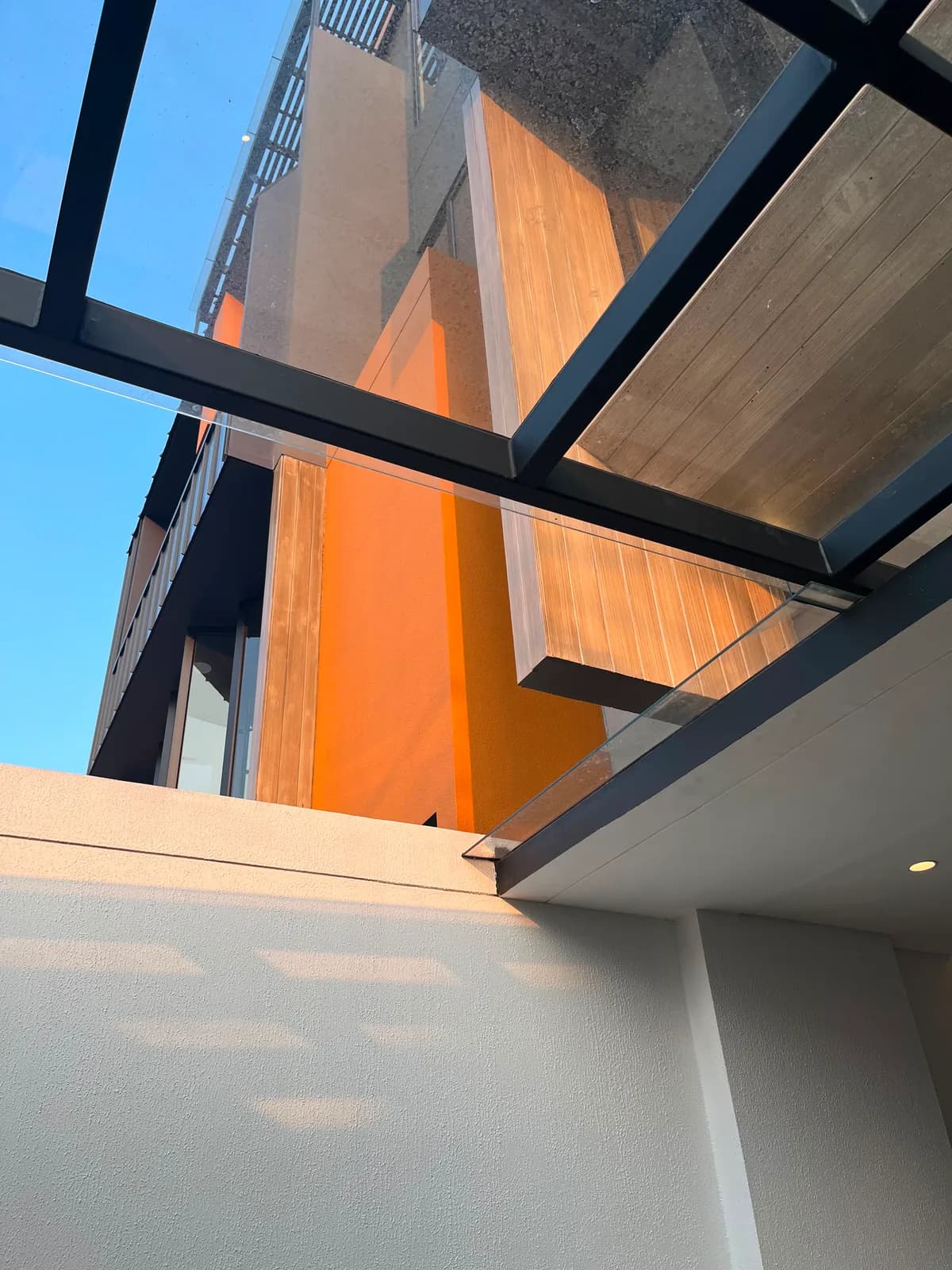 The upper floors seen from below: orange plaster, timber cladding and black-framed glass