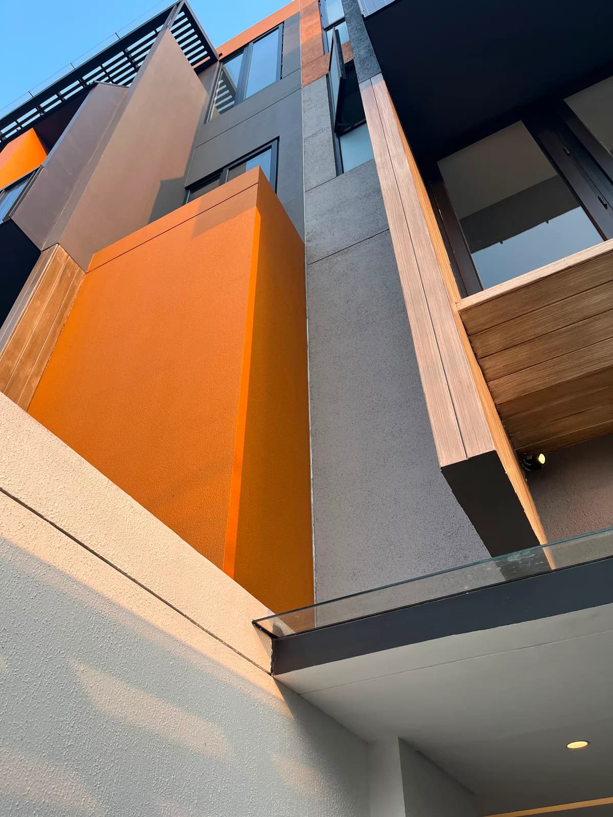 Upward view of the front facade: an orange plastered panel, grey stone and timber cladding
