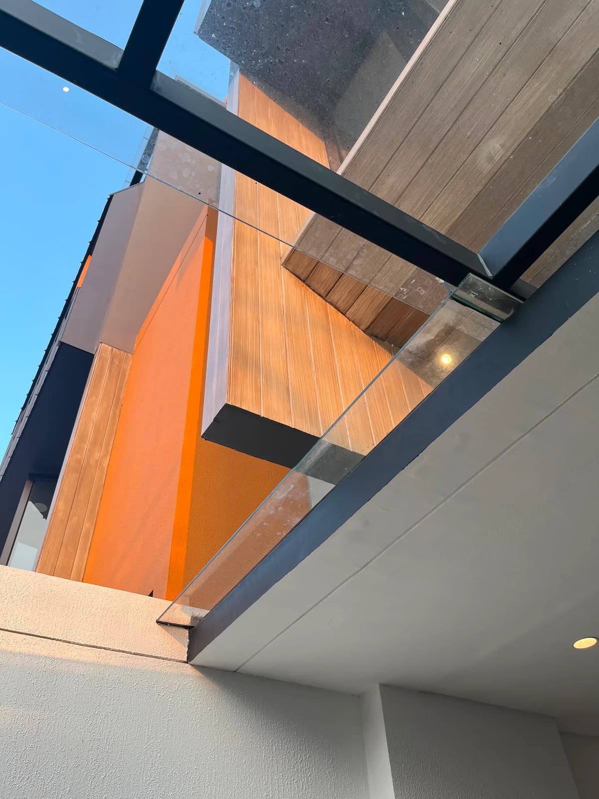 Looking up at the timber-lined soffit, the orange plastered wall and a glass balustrade